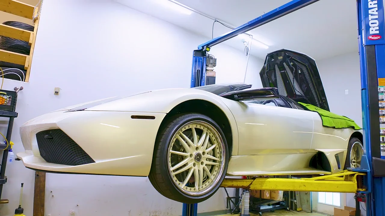 A white Lamborghini Murciélago raised on a two-post lift inside the shop